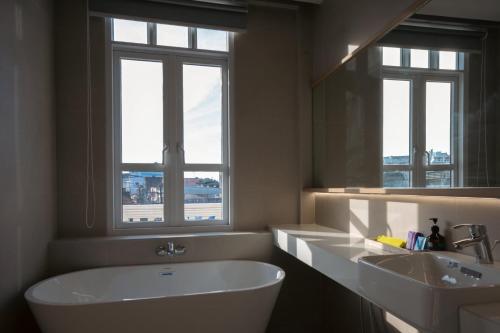 a bathroom with a tub and a sink and two windows at GinGin Hotel, Trang Old Town in Trang