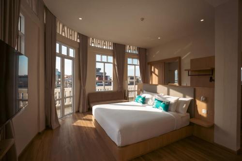 a bedroom with a large white bed and large windows at GinGin Hotel, Trang Old Town in Trang