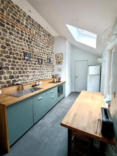 a kitchen with a wooden table and a brick wall at Le Cinquante-Trois, Maison Normande d'exception pour familles - Côte d'Albâtre in Saint-Valery-en-Caux