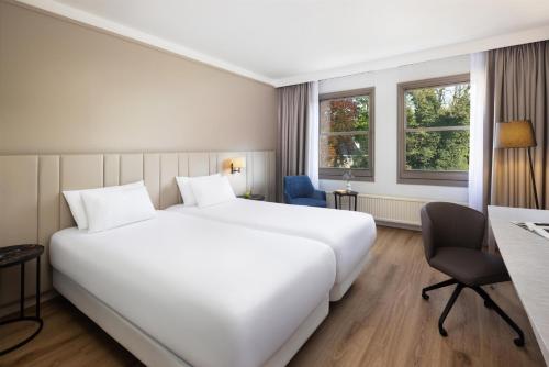 a hotel room with a large white bed and a desk at NH Bussum Jan Tabak in Bussum