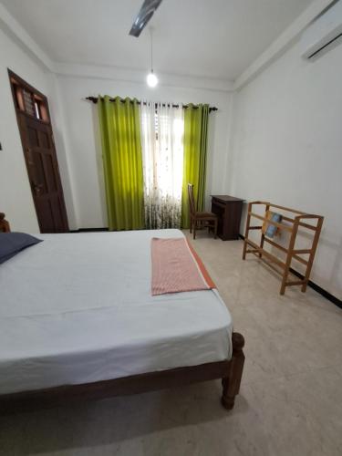a bedroom with a bed and a window with green curtains at Home mr in Matara