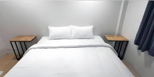 a bed with white sheets and two wooden tables at xx GO INN Phuket old Town in Ban Lo Long