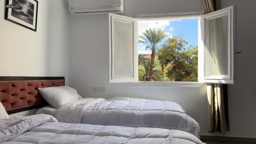 a bedroom with two beds and a window with a palm tree at TriPyramids Suites in Cairo