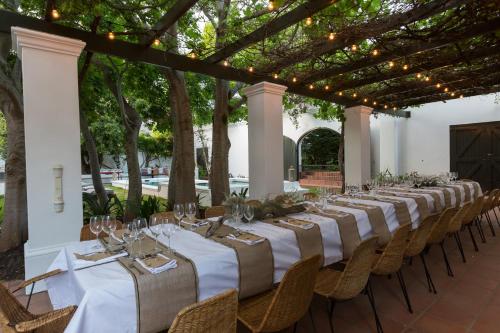 a long table with white tables and chairs under a pergola at Akademie Street Boutique Hotel in Franschhoek