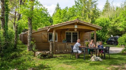 a family sitting at a table in front of a cabin at Camping nature 3 étoiles - au coeur des montagnes du Jura in Levier