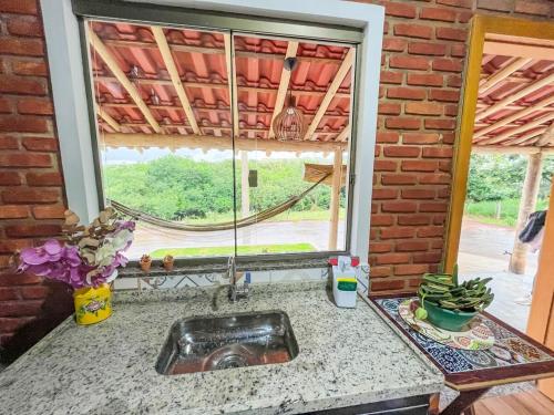 a kitchen counter with a sink and a window at Chalé Flor de Ypê in Carrancas