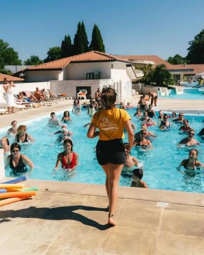 a woman walking in a swimming pool with a group of people at ZEcamping 4 étoiles avec parc aquatique - sauna et hammam in Sanguinet