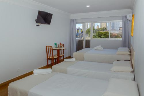 a room with three beds and a table with a window at Harbor Buriti Hotel in Campo Grande