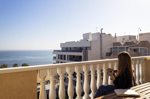 a woman sitting on a balcony looking at the ocean at Penthouse Pink seafront in La Mata