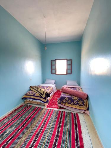 two beds in a blue room with a rug at Sahara desert Maison in Merzouga