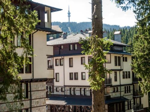 a group of buildings with a tree in the foreground at Green Life Family Apartments Pamporovo in Pamporovo