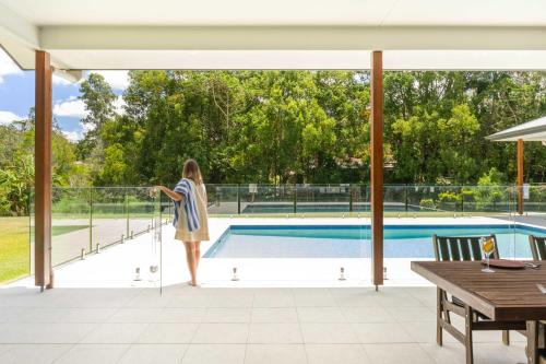 a woman standing on a balcony overlooking a swimming pool at Hinterland Haven with Heated Pool & Lush Surrounds in Mooloolah