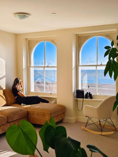 a woman sitting on a couch in a room with windows at Ocean Whisper - 2 Bedroom Sea Front Apartment in Folkestone