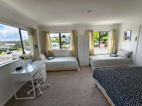 a bedroom with two beds and a desk and windows at Sweet North Cote Stay in Auckland