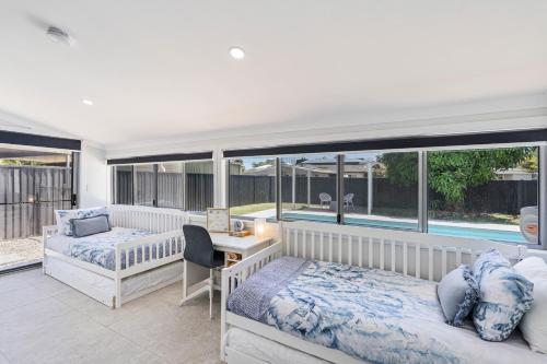 a bedroom with two beds and a desk and windows at Pet Friendly Beach House with pool - Sleeps 10 in Urangan