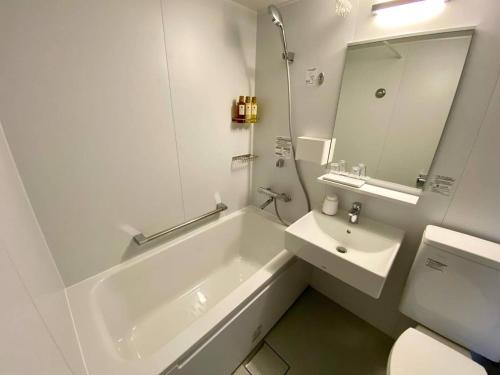 a white bathroom with a tub and a sink at ライベストイン奄美アネックス in Koniya
