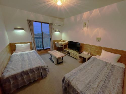 a hotel room with two beds and a television at Pension KUROSHIOMARU in Setouchi