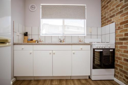 a kitchen with white cabinets and a brick wall at Bayview Motel in Esperance