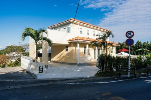 a white building with palm trees in front of a street at Villala Fibana in Motobu