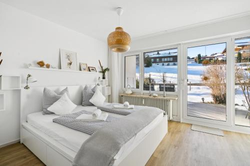 a white bedroom with two beds and a large window at Schneerosenblüte Steibis mit O Plus in Oberstaufen