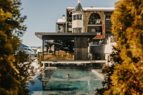 a person swimming in a pool in front of a building at Alpin Garden Luxury Maison & SPA - Adults Retreat in Ortisei