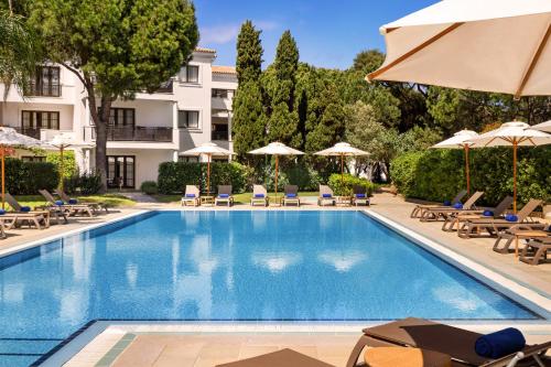 a swimming pool with chairs and umbrellas next to a building at Pine Cliffs Suites in Albufeira