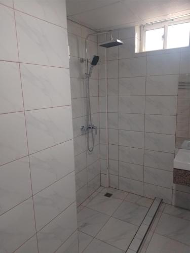 eine Dusche in einem weiß gefliesten Badezimmer mit Fenster in der Unterkunft Atlas Hotel in Arusha