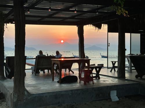 two people sitting at a table on the beach at sunset at Phayamhostel in Ko Phayam