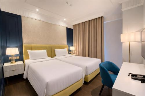 a hotel room with two beds and a blue chair at Maia Hotel Jakarta in Jakarta