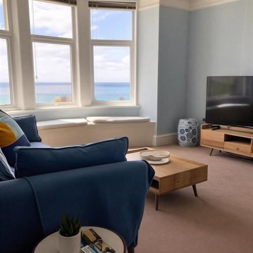 a living room with a blue couch and a television at Spacious flat - fabulous sea views & walk to beach in Woolacombe