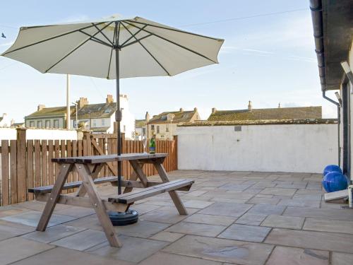 a picnic table with an umbrella on a patio at Porthole Cottage in Allonby