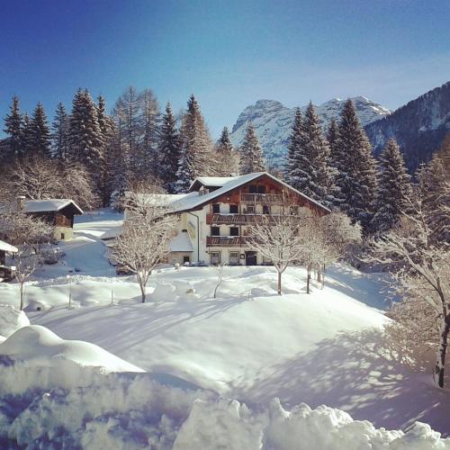 a building in the snow with trees and mountains at Rifugio Caltena in Fiera di Primiero