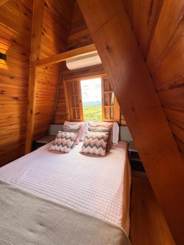 a bed in a wooden room with a window at Vale dos Ventos - Chalés e Hospedagem in Jaboticatubas