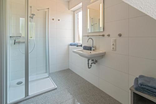 a white bathroom with a shower and a sink at Ferienhaus Empora in Bensersiel