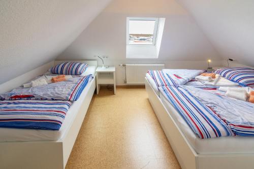 two twin beds in a attic bedroom with a window at Ferienhaus Avantgarde in Neuharlingersiel