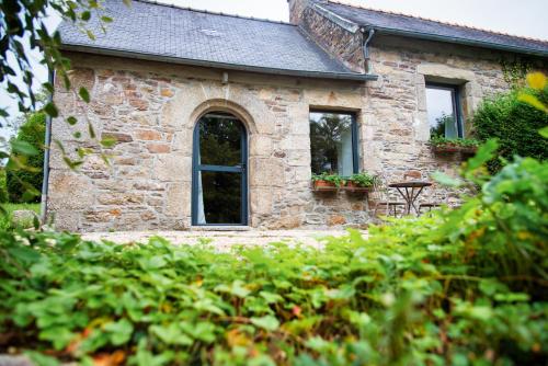 a stone house with two windows and some bushes at Domaine le Puits de Jeanne in Plouégat-Moysan
