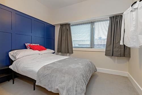 a bedroom with a bed with a blue headboard and a window at PRIME CITY CENTRE MK STAY, Stylish Spacious Apartment, AIR CONDITIONG, Two bathrooms, FREE GATED ALLOCATED PARKING & Lift access in Milton Keynes