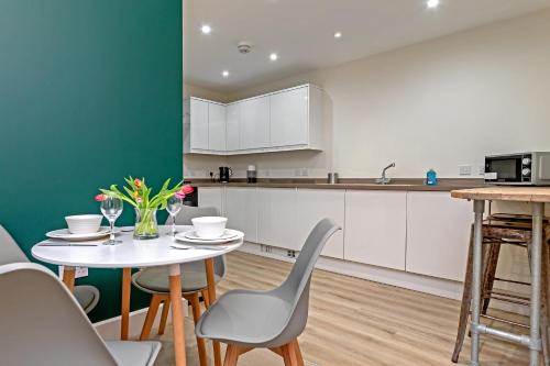 a kitchen with white cabinets and a table and chairs at PRIME CITY CENTRE MK STAY, Stylish Spacious Apartment, AIR CONDITIONG, Two bathrooms, FREE GATED ALLOCATED PARKING & Lift access in Milton Keynes