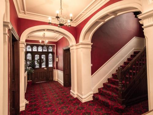 a hallway with red walls and stairs with a chandelier at Elim Bank Guest House in Windermere