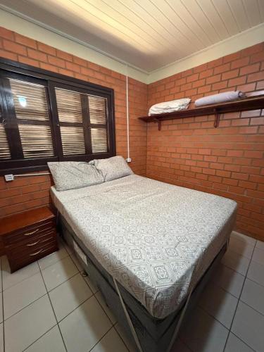 a bed in a room with a brick wall at Casa praia bella torres in Passo De Torres