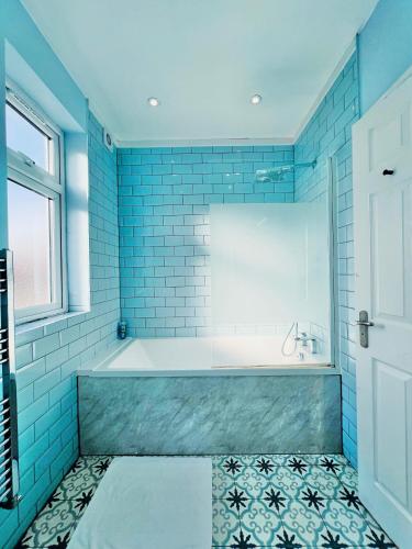 a bathroom with a tub and blue tiles at Gants Hill House in Redbridge