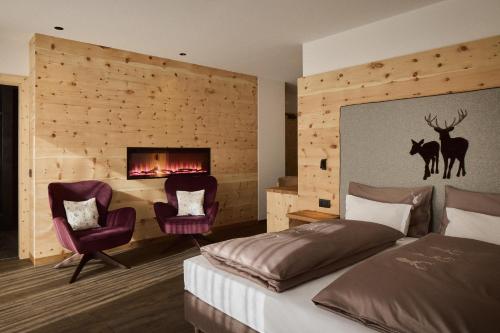 a bedroom with a bed and two chairs and a fireplace at Hotel Mesdi in Arabba