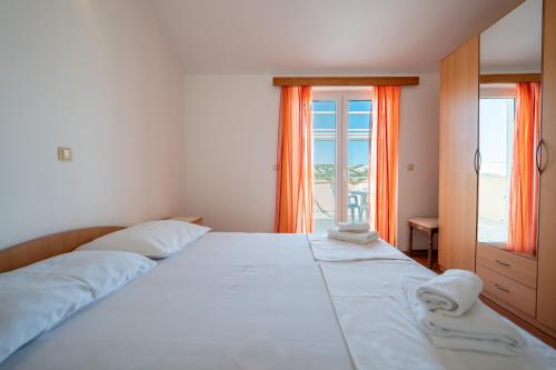 a bedroom with a large white bed with orange curtains at Apartmani Kaštel in Stara Novalja