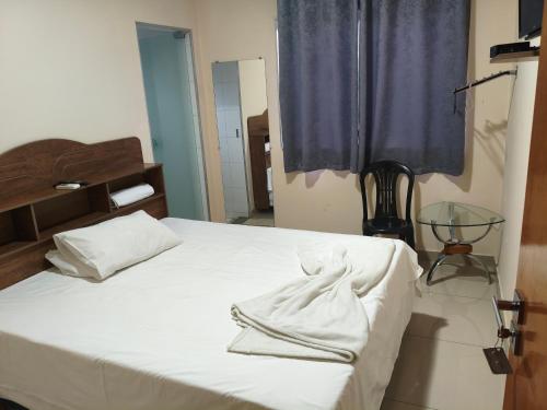 a bedroom with a bed with white sheets and a window at Hotel Mourão in Guanhães