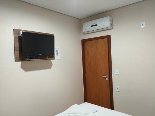 a room with a bed and a television and a door at Hotel Mourão in Guanhães