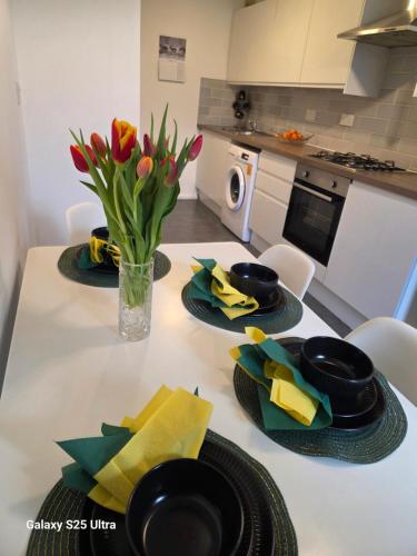 a kitchen table with two plates and a vase of flowers at Green & White Haven-Spacious 3BR in London