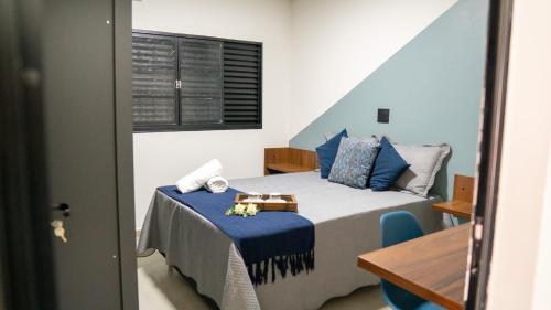 a bedroom with a bed with blue pillows and a table at Jahu Center Casas Un 4 in Jaú