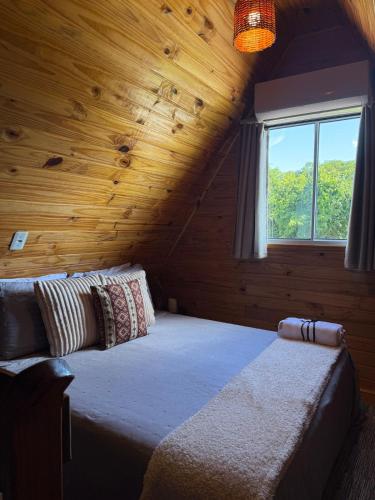 a bed in a wooden room with a window at Cabanas Paxixi - Mirante in Camisão