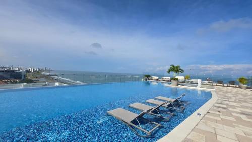 a swimming pool with lounge chairs and the ocean at Luxury Oceanfront Apartment Spiaggia 2BR 3BA Playa azul Cartagena in Cartagena de Indias