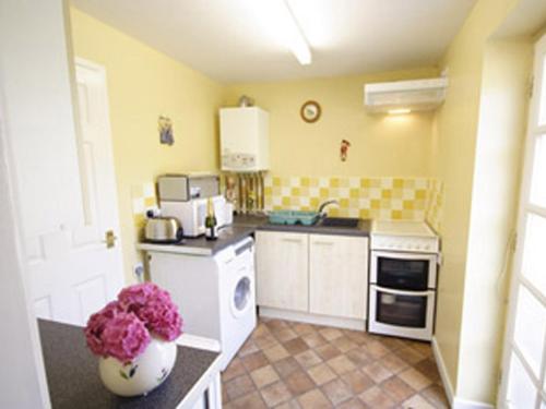 a kitchen with yellow walls and white cabinets and pink flowers at Wisteria Cottage in Aylsham